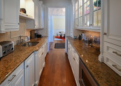 A kitchen with white cabinets and brown granite counter tops.