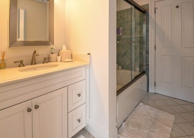 A bathroom with white cabinets and a glass shower door.